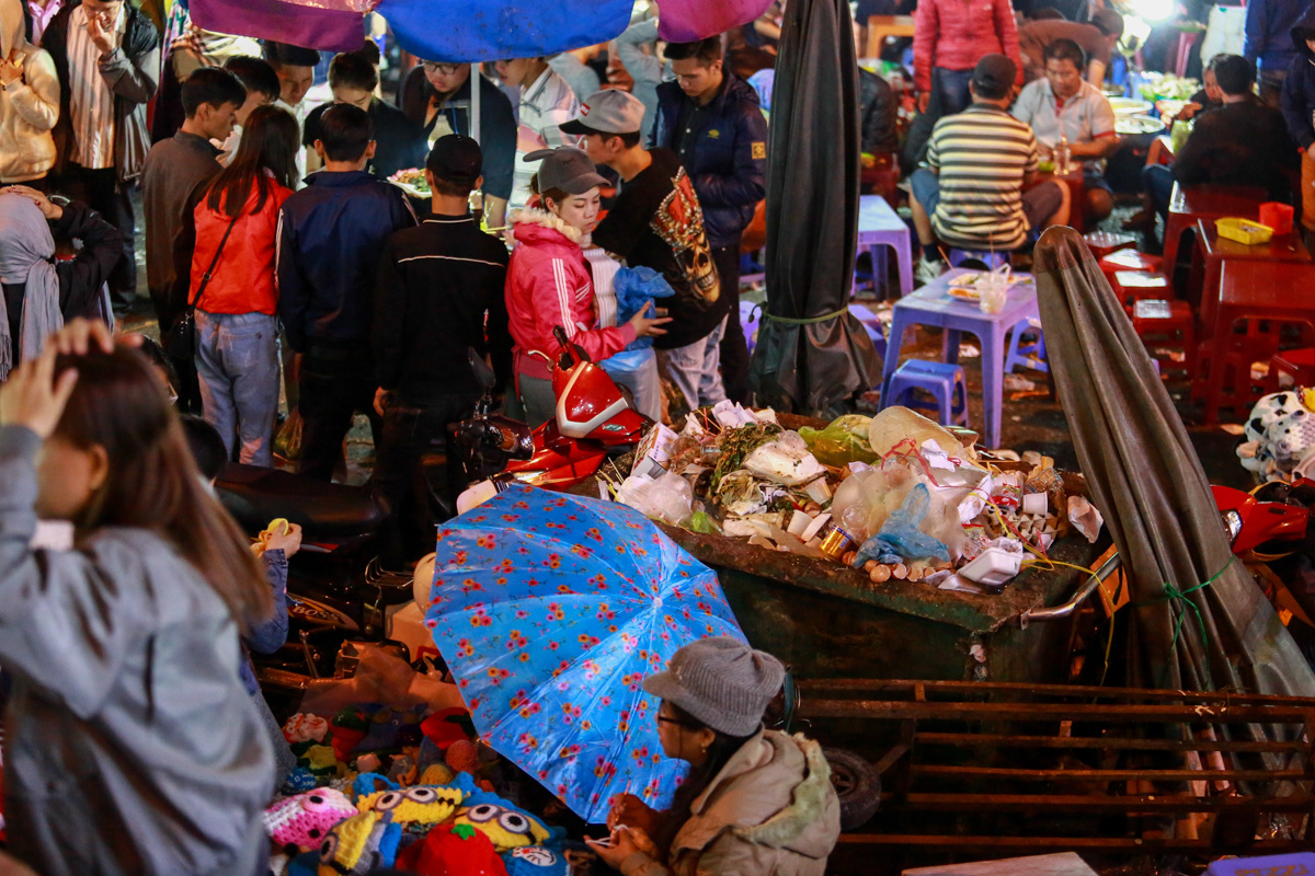 Một thùng rác chất đầy rác đặt bên cạnh các quán ăn, cửa hàng buôn bán tại chợ Đà Lạt.