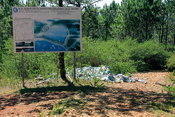 Bên dưới tấm bảng dự an vệ sinh hồ lắng đầu nguồn hồ Chiến Tháng là cả đống bao bì thải loại